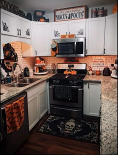 a kitchen decorated for halloween with white cabinets, black appliances and orange decorations on the wall