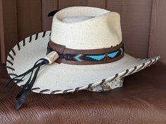 The Maverick starts with a Mexican soft palm leaf hat body that has a 3 3/4" brim and 5 1/4" crown. Hand laced in chocolate brown leather lace. The beaded hatband has a Thunderbird pattern and then mounted on distressed leather. The back of the band has a deer antler bead for accent. Starburst turquoise Concho and deep blue/green decorative feather completes the hat. All hats are made to order. Allow up to 4 weeks for your hat to ship. Brown Toquilla Straw Hat Bands For Ranch, Western Style Brown Panama Hat With Flat Crown, Brown Toquilla Straw Hat Band For Western-themed Events, Rustic Natural Hat Bands For Western-themed Events, Western Brown Panama Hat With Flat Crown, Traditional Hats With Short Brim For Western-themed Events, Traditional Short Brim Hat For Western-themed Events, Fitted Brown Straw Hat For Western-themed Events, Brown High Crown Fedora For Country Events