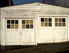 an old white garage with two doors and windows on the side of it in front of a building