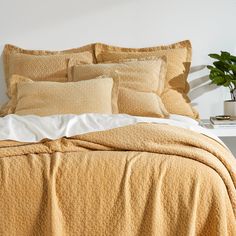 a bed with yellow sheets and pillows in a white room next to a potted plant