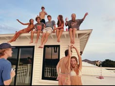 a group of people hanging out on top of a house with their hands in the air