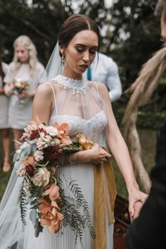 a bride and groom holding hands in front of other people wearing wedding gowns with flowers on them