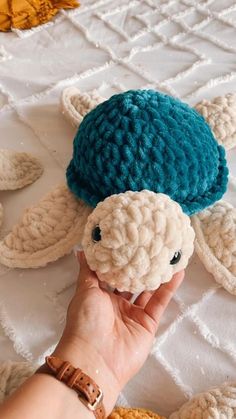 a hand holding a stuffed turtle on top of a white table cloth covered with crochet