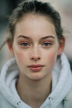 a woman with freckled hair and blue eyes looks at the camera while wearing a white hoodie