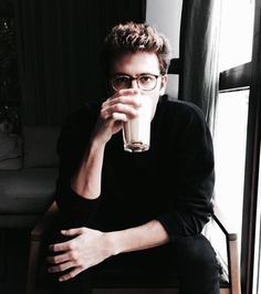 a man sitting in a chair drinking from a tall glass with his hand on his chin