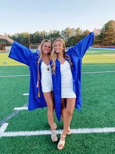 two girls in graduation gowns standing on a field