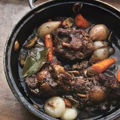 a pot filled with meat and vegetables on top of a wooden table