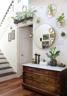 a wooden dresser sitting under a mirror next to a stair case with potted plants on it