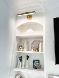 a white shelf with vases, books and other items on it in a room