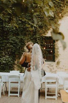 a bride and groom kissing in front of an ivy covered building with white folding chairs