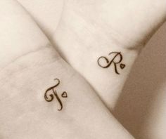 two small tattoos on the arms of someone's arm and wrist, both with initials