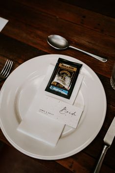 a white plate topped with a card on top of a wooden table next to silverware