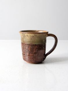 a brown and green coffee cup sitting on top of a table next to a white wall