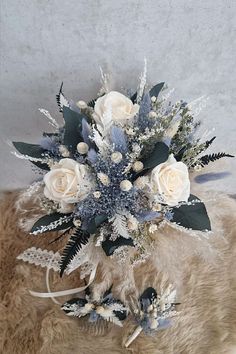 a bridal bouquet with white roses and blue foliage on a fur rug in front of a wall