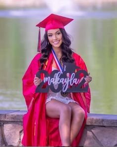 a woman in a graduation cap and gown sitting on a stone wall holding a sign