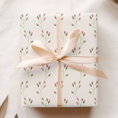 a gift wrapped in white paper with pink flowers on it next to utensils