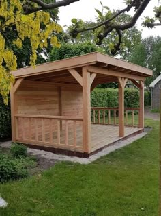 a wooden gazebo sitting in the middle of a lush green field next to a tree