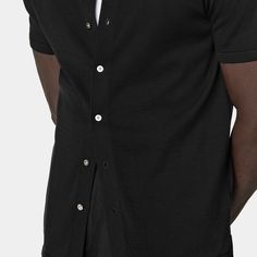 A perfect way to elevate any casual look, this black short-sleeve polo cardigan features a classic polo collar, a seven-button closure, and a slim, tapered silhouette for a sleek aesthetic. Black Polo Shirt With Button Closure For Work, Casual Top With Hidden Button Closure, Black Polo Shirt With Johnny Collar For Work, Workwear Polo Collar Top With Buttons, Black Short Sleeve Polo Shirt For Work, Black Shirt With Hidden Button Closure For Business Casual, Formal Polo Collar Top With Button Closure, Fitted Polo Shirt With Button Closure For Business Casual, Fitted Button-up Polo Shirt For Business Casual