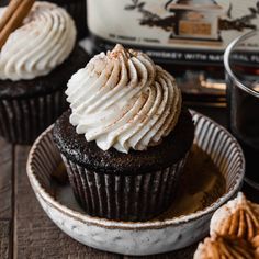 two chocolate cupcakes with whipped cream on top and cinnamon sticks in the background