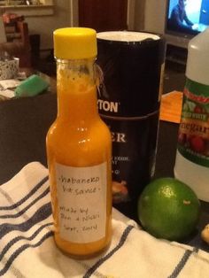 a bottle of hot sauce sitting on top of a table next to limes and an orange