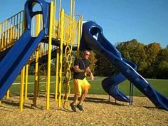 a man standing next to a blue and yellow playground structure with slide in the background