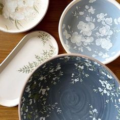 three bowls with flowers painted on them sitting on a wooden table next to each other