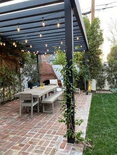 outdoor dining area with climbing vines on black wood pergola Garden Design Pergola, Outdoor Pergola With Vines, Vines Landscaping, Black Pergola White House, Outdoor Brick Wall, Brick House Pergola, Pergola With Ivy, Brick House With Pergola, Vine Over Pergola