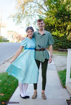 a man and woman dressed in costume posing for a photo on the sidewalk with trees behind them