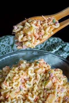 two wooden spoons with macaroni and cheese on them in a glass bowl