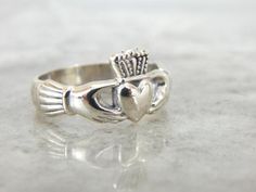 a silver cladder's ring with a heart and crown on the front, sitting on a white surface