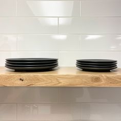 three black plates sitting on top of a wooden shelf next to a white tiled wall