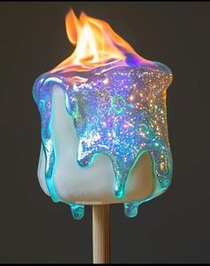 a lit candle with blue and yellow fire on it's side, sitting on a stick