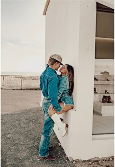 a man and woman leaning against the side of a white building with their arms around each other