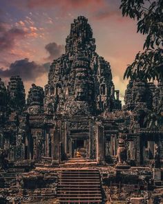 an ancient temple with steps leading up to it and trees in the foreground at sunset