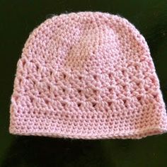 a pink knitted hat sitting on top of a wooden table next to a black surface