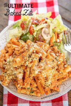 a white plate topped with pasta covered in cheese and sauce next to a salad on a checkered table cloth