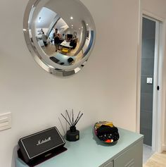 a mirror is hanging on the wall above a dresser with a speaker and other items