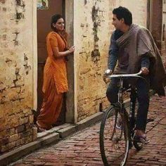 a man riding a bike down a street next to a woman in an orange dress