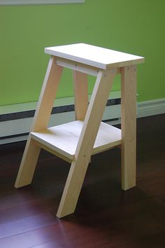 a small wooden step stool sitting on top of a hard wood floor next to a green wall