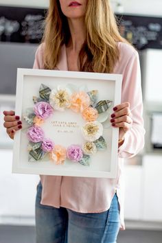 a woman holding up a framed photo with flowers on it