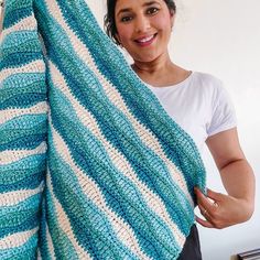 a woman holding up a blue and white crocheted blanket