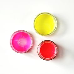 three small jars filled with different colored paints on top of a white table next to each other