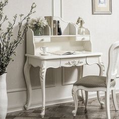 a white desk with a mirror, chair and vase on it next to a wall