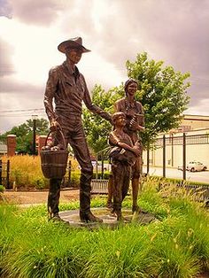 a statue of two men shaking hands in front of a train station with green grass