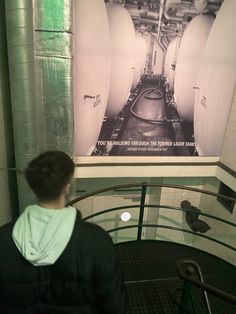 a man standing in front of a poster on the wall next to a stair case