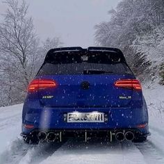 the rear end of a blue car driving on a snow covered road with trees in the background