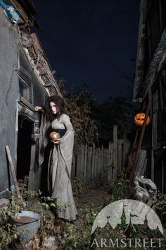 a woman dressed as a witch holding a pumpkin in front of an old house at night