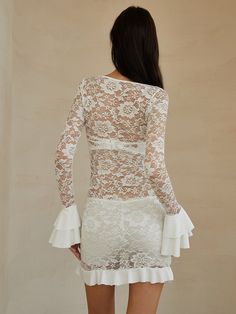 the back of a woman wearing a white dress with long sleeves and frills