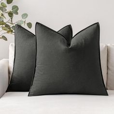 two black pillows sitting on top of a white couch next to a potted plant