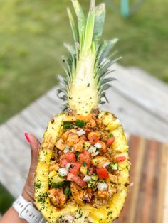 a person holding up a pineapple with food on it